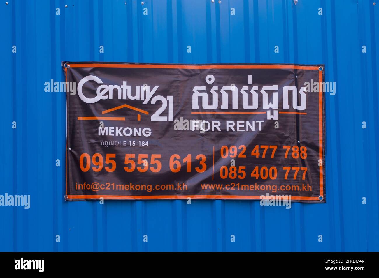 Aufgrund der COVID - 19 Epidemie befindet sich Phnom Penh in einer Wirtschaftskrise. In der ganzen Stadt sind „zur Miete“- und „zum Verkauf“-Schilder zu sehen. Während der Coronavirus-Pandemie hängt ein zweisprachiges Schild aus dem Jahr 21 an einer frisch bemalten blauen Wand. Stueng Meanchey, Phnom Penh, Kambodscha. April 2021. © Kraig Lieb Stockfoto