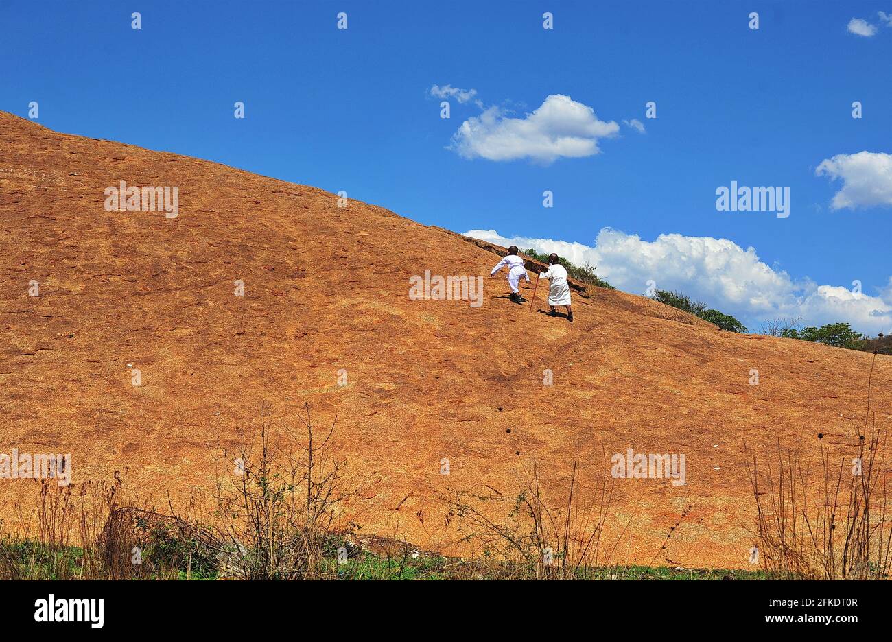 Afrikanische Gläubige, die in Limpopo, Südafrika, einen felsigen Hügel hinaufgehen, um an einem klaren Tag mit blauem Himmel zu beten Stockfoto