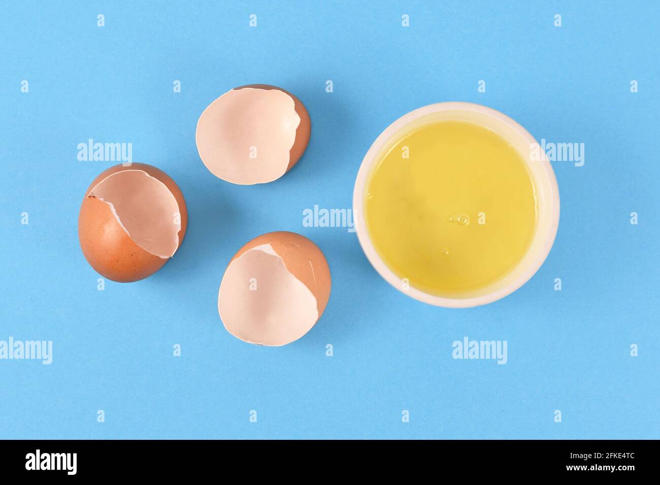 Eiweiß in der Schüssel neben zerbrochenen Eierschalen auf Gelb Hintergrund Stockfoto