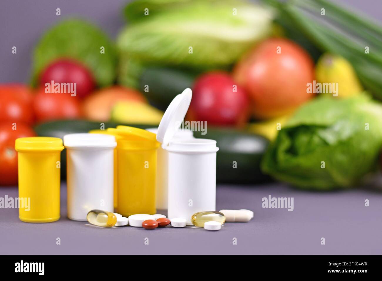 Flaschen mit Nahrungsergänzungsmitteln Pillen vor Früchten Und Gemüse im Hintergrund Stockfoto