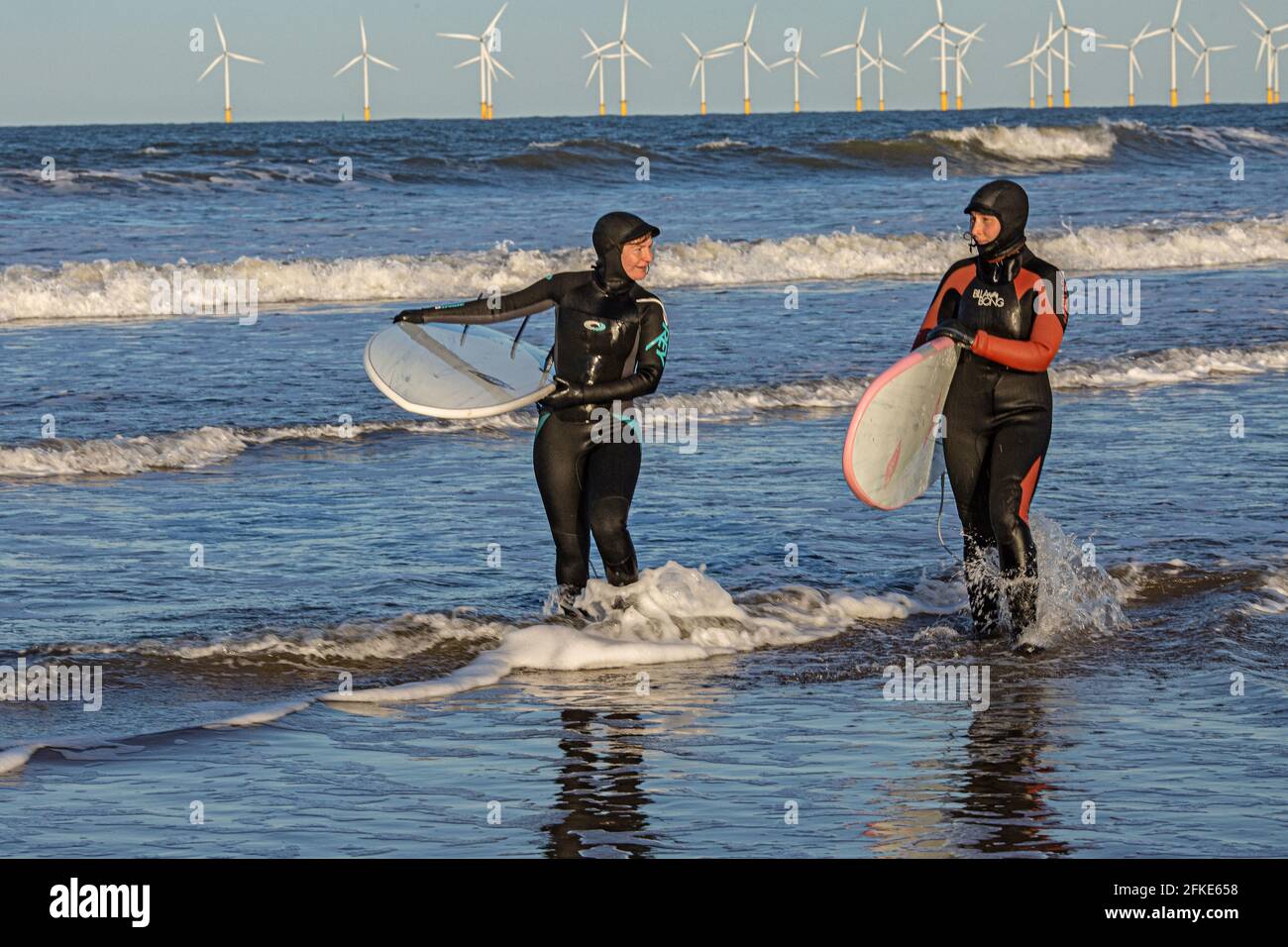 Olivia Harris (links) und ihre Freundin Rachel surfen in Seaton mit Teesside Offshore Windfarm in der Ferne. England, Großbritannien Stockfoto