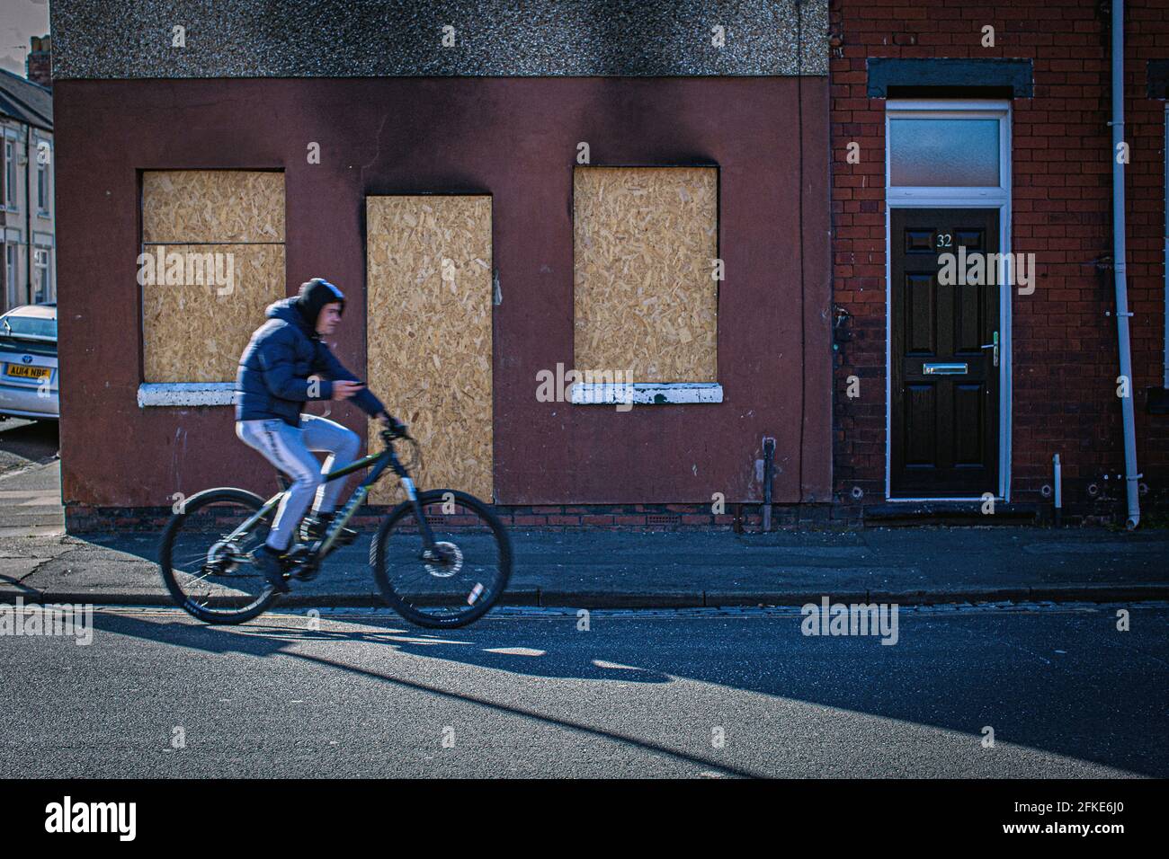 Mann auf dem Fahrrad, der an Fenstern und Türen in den am stärksten benachteiligten Straßen vorbeiging, die sich um das Stadtzentrum in Hartlepool, County Durham, Großbritannien, befinden Stockfoto