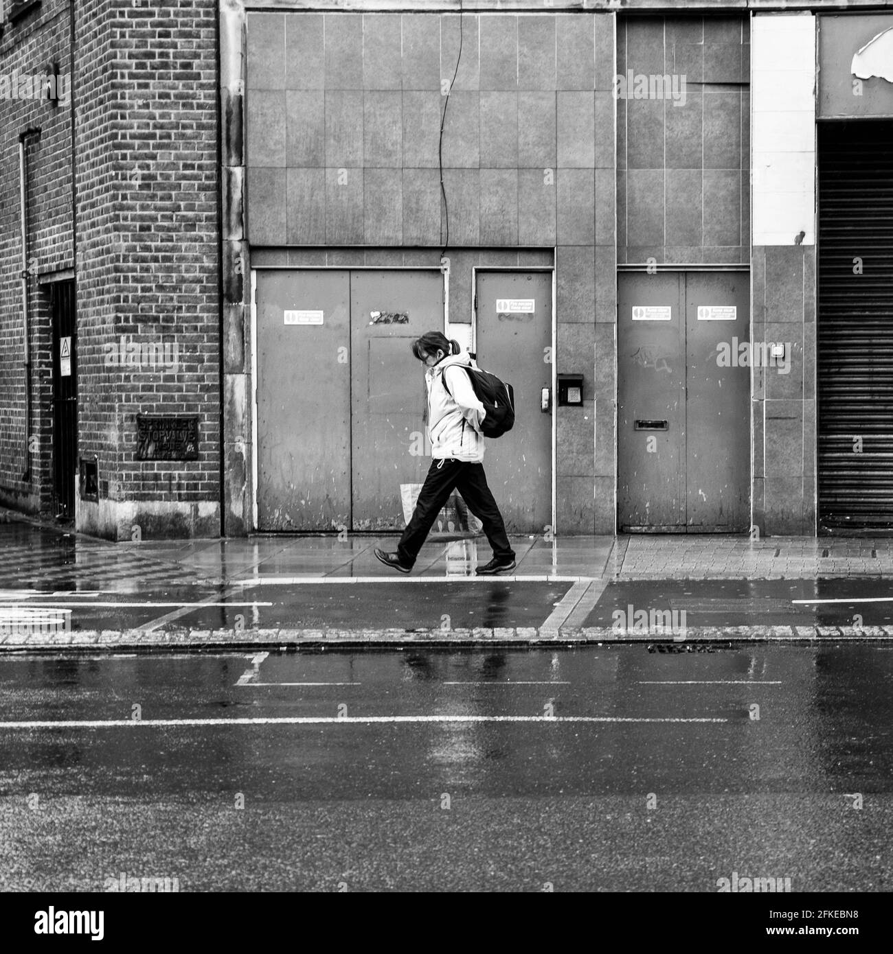 Kingston upon Thames, London, Großbritannien, Frau, die an EINEM verwelkenden Gebäude in The Rain vorbeigeht Stockfoto