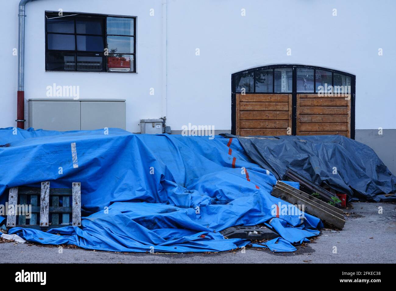 Objekte einer Baustelle vor einem Haus sind mit einer großen blauen Schutzplane bedeckt. Stockfoto