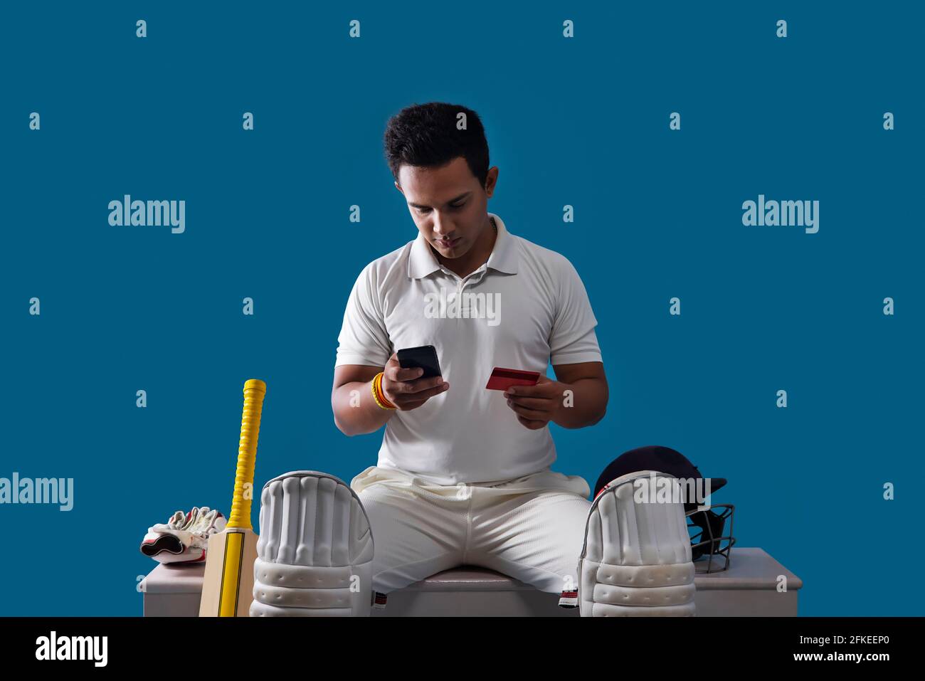Ein Batsman, Cricketspieler, der in der Garderobe sitzt und Online-Shopping macht Stockfoto
