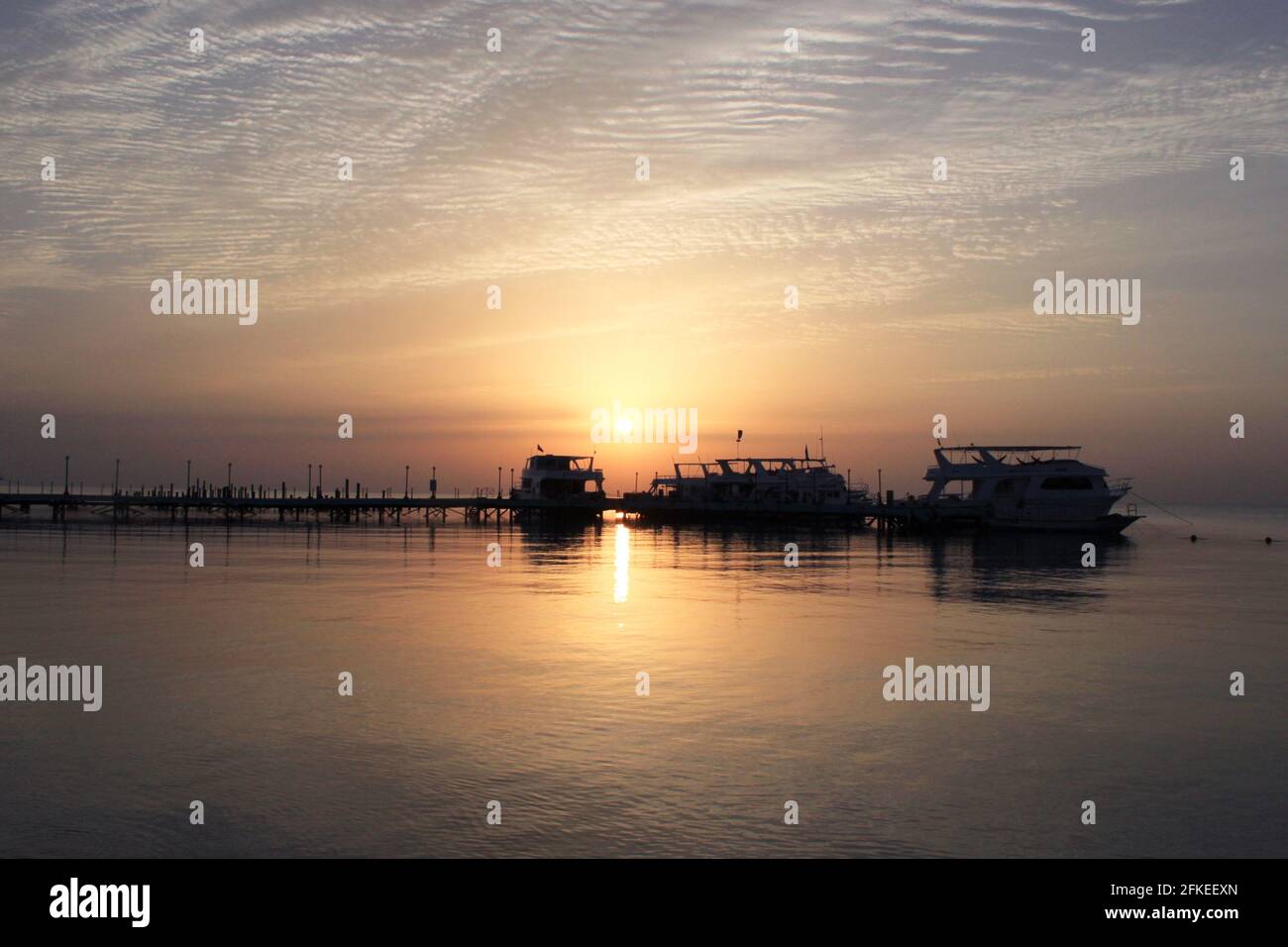 Sonnenaufgang auf dem Meer. Pier und Boote auf dem Wasser. Pier und Yachthafen mit Booten. Spiegelung der Sonne im Wasser. Rotes Meer, Safaga, Ägypten. Stockfoto