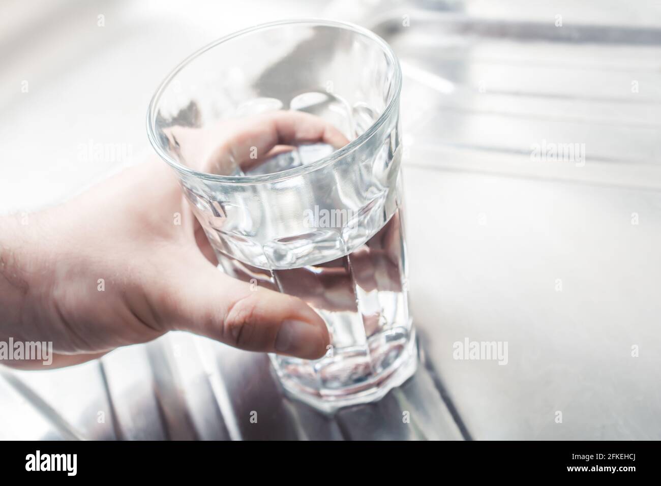 Hand ein mit Wasser gefülltes Trinkglas anhalten Ein Küchenwaschbecken Stockfoto