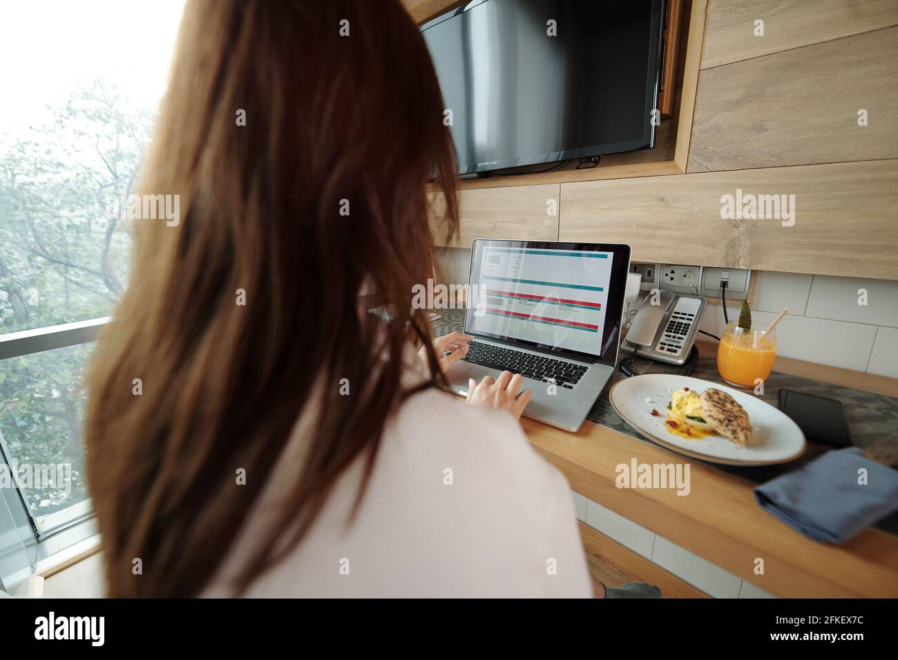 Junge Frau, die Frühstück isst, Flug bucht und Ticket auf dem Laptop kauft, Blick über die Schulter Stockfoto