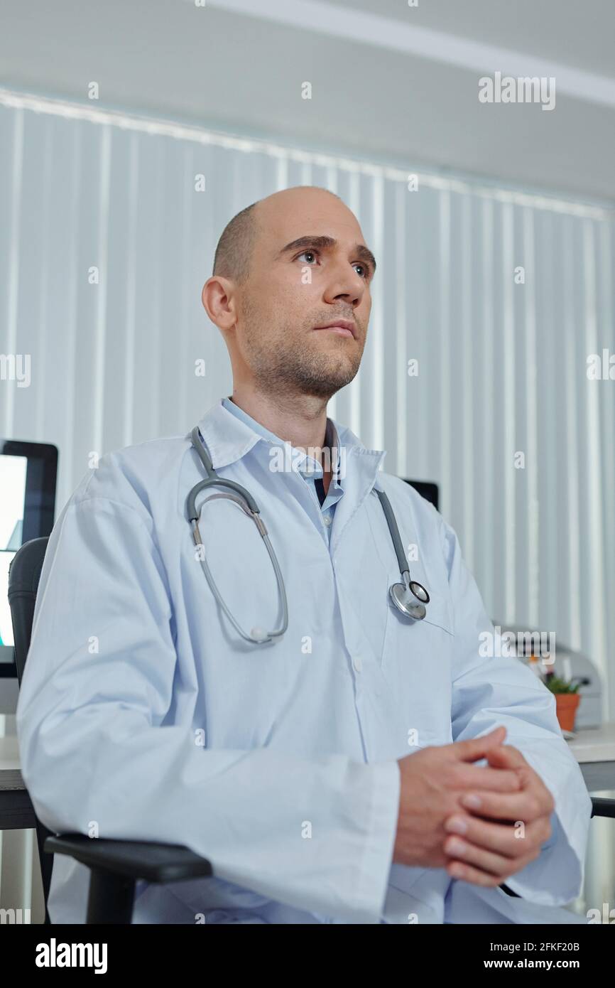 Porträt eines gutaussehenden ernsthaften Hausarztes, der eine Pause im Aufenthaltsraum der Ärzte verbringt, denkt er an die Diagnose des Patienten Stockfoto