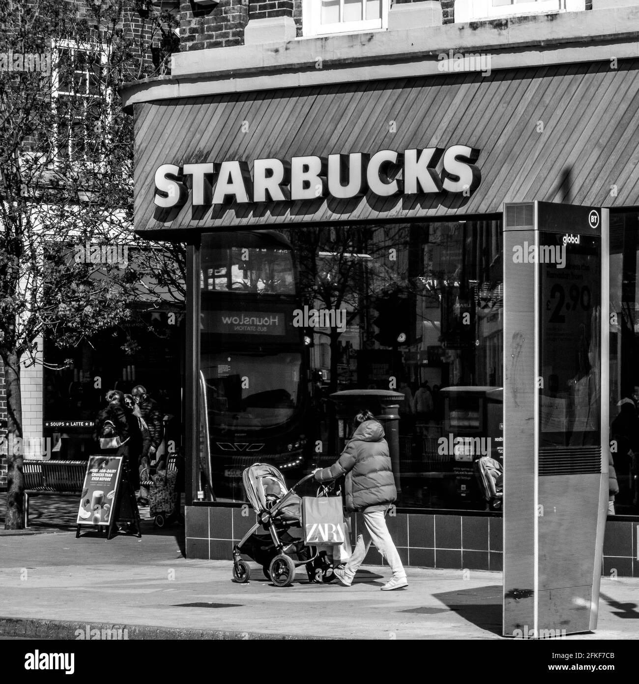Kingston upon Thames, London, Großbritannien, April 2021, Frau, die an EINEM Starbucks Coffee Shop vorbeigeht und einen Kinderwagen oder Kinderwagen schiebt Stockfoto