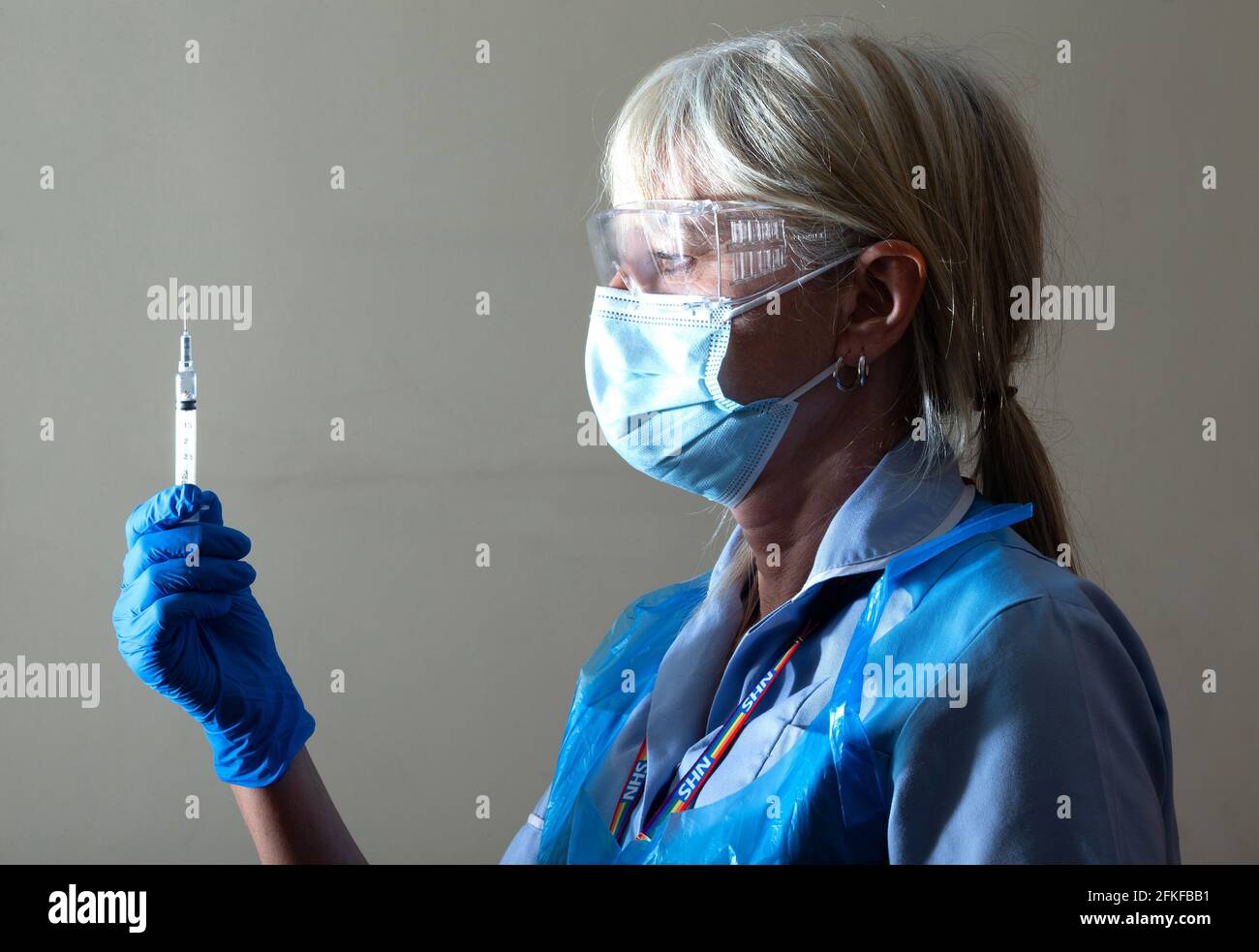 Eine NHS-Krankenschwester überprüft eine Nadel mit einer Dosis des Covid-Impfstoffs und verabreicht dann den ersten Impfstoff. Stockfoto