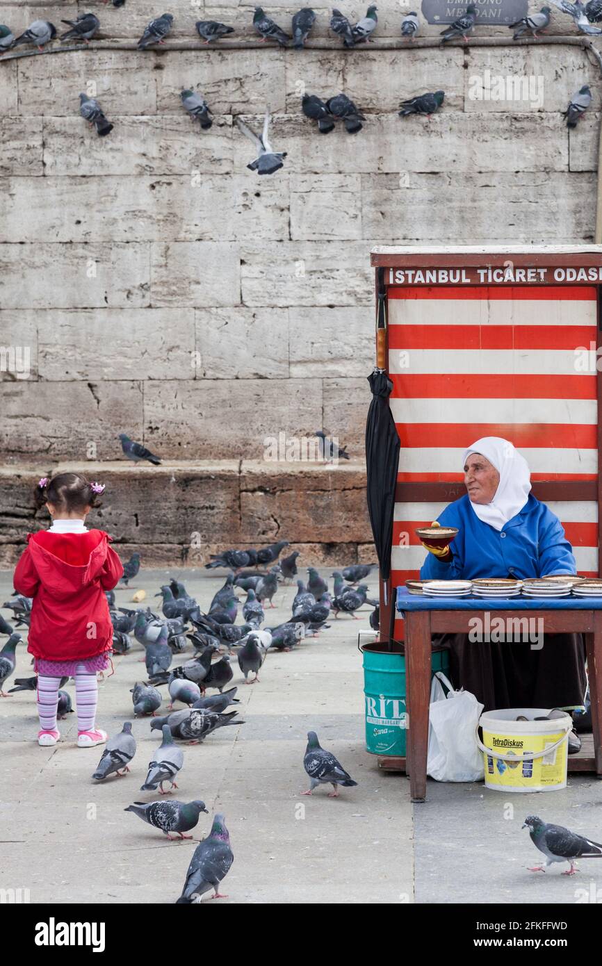 Ältere Frau verkauft Vogelfutter mit jungen Mädchen, die Tauben füttern In Istanbul Stockfoto