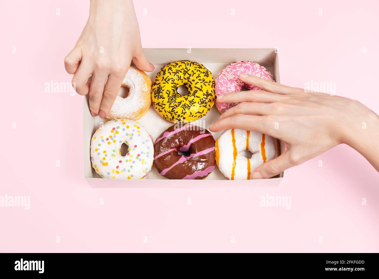 Hände nehmen farbige glasierte Donuts in Donut-Box. Hände greifen verschiedene Geschmacksrichtungen Donuts. Ungesunde Snacks im Büro oder in einer Pausenstation. Stockfoto