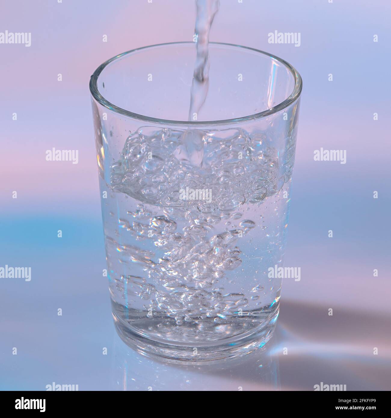 Wasser fließt in Glas. Neonlichter Farbästhetik Stockfoto