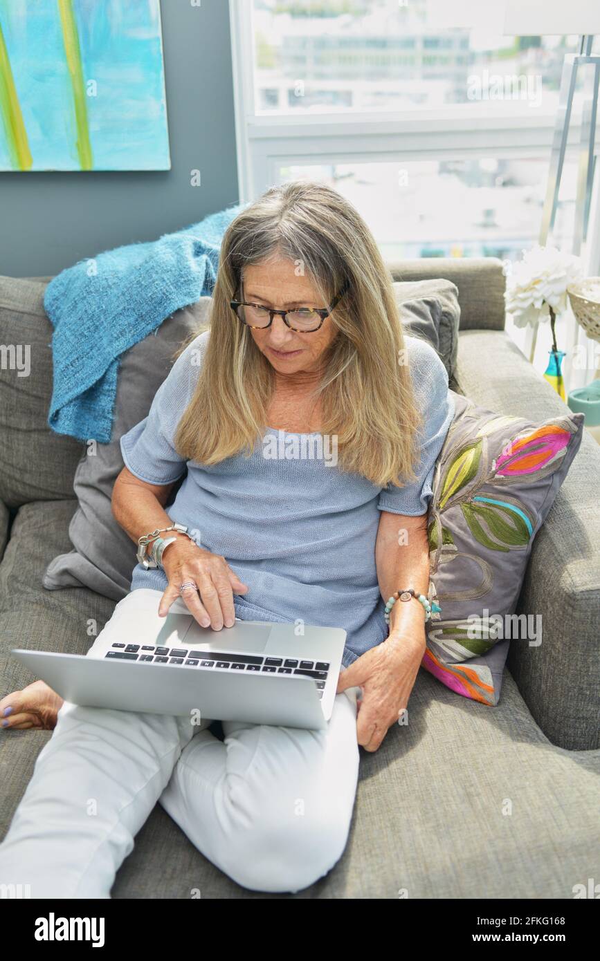 Attraktive ältere Frau, die auf dem Sofa am Computer arbeitet Stockfoto