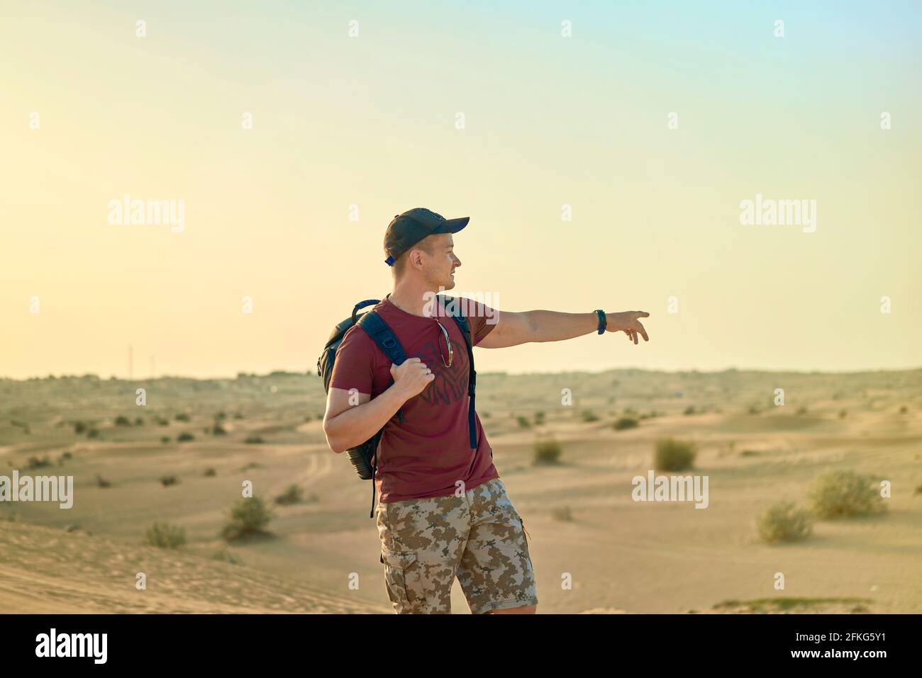 Rückansicht eines männlichen Touristen in einer Sonnenbrille mit Rucksack beim Bummeln Unter der Sonne entlang der Sanddünen und mit Blick auf die Wüste Landschaft Stockfoto