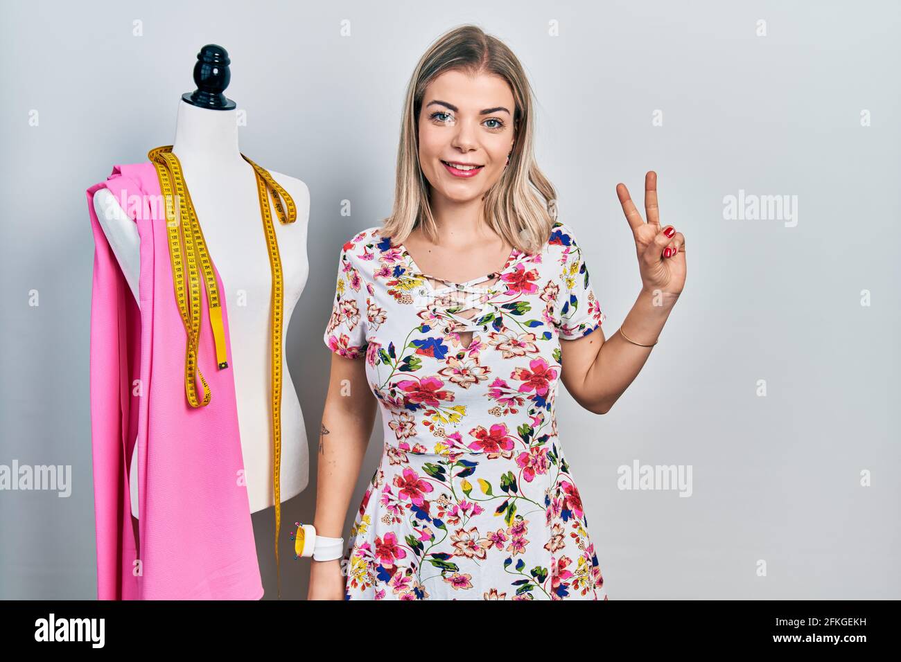 Schöne kaukasische Frau Schneiderin Designer von menschlich lächelnd mit glücklichen Gesicht zwinkerte an der Kamera tun Siegeszeichen. Nummer zwei. Stockfoto