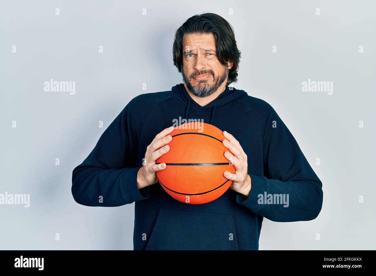 Mittleren Alters kaukasischen Mann hält Basketball Ball ahnungslos und verwirrt Ausdruck. Zweifel Konzept. Stockfoto