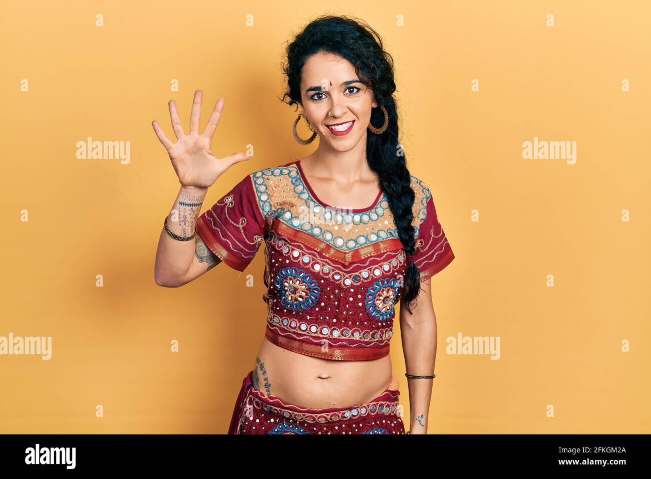 Junge Frau in Bindi- und bollywood-Kleidung zeigt und zeigt mit den Fingern Nummer fünf auf, während sie selbstbewusst und glücklich lächelt. Stockfoto
