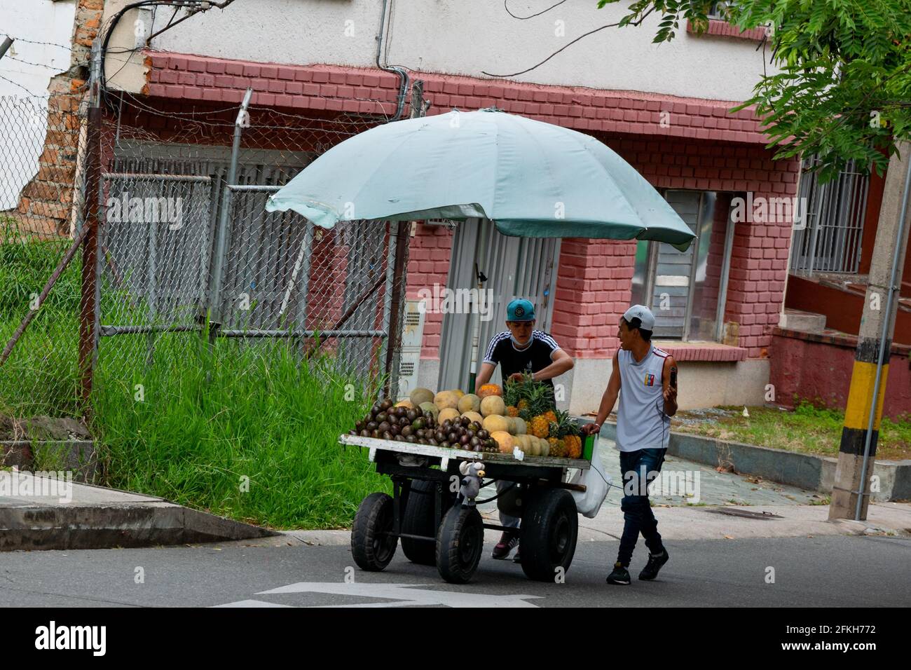 Medellin, Kolumbien - März 28 2021: Junge Männer, die Avocados, Ananas und Melone in einem Regenschirmwagen verkaufen Stockfoto