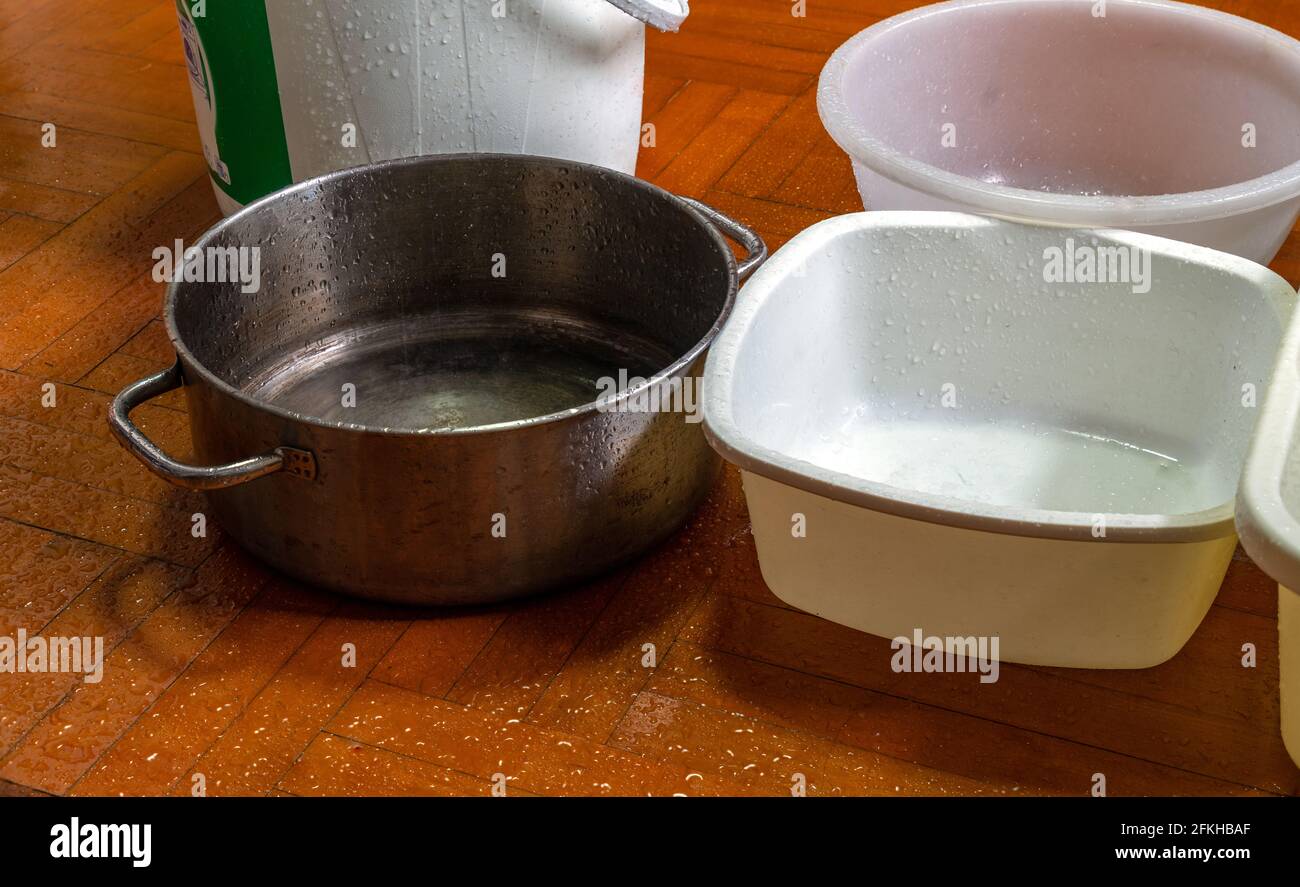 Verschiedene Container auf dem Holzboden des Hauses angeordnet. Zur Aufnahme von Regenwasser, das bei starkem Regen vom Dach austritt. Stockfoto