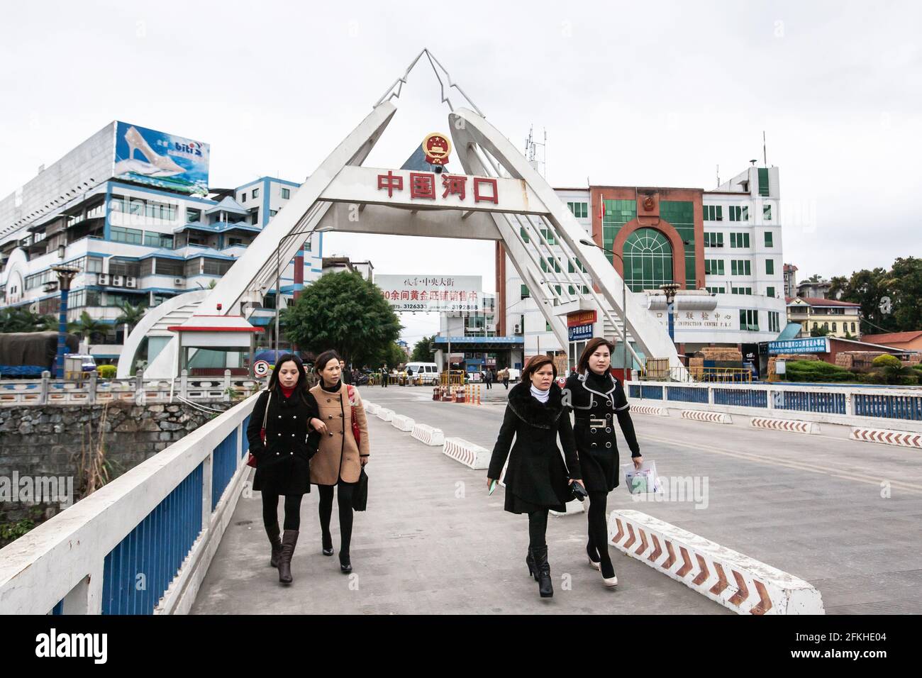 Lao Cai, Vietnam – 29. FEBRUAR 2012: Asiatische Frauen in langen Mänteln überqueren die Brücke über den Roten Fluss von Hekou, China (Hintergrund). Vietnam. Stockfoto