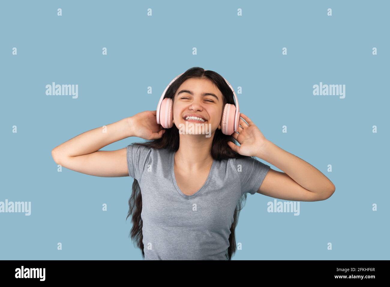 Fröhlicher indischer Teenager in modernen kabellosen Kopfhörern, der beliebte Lieder in der Audio-App genießt und Musik hört Stockfoto