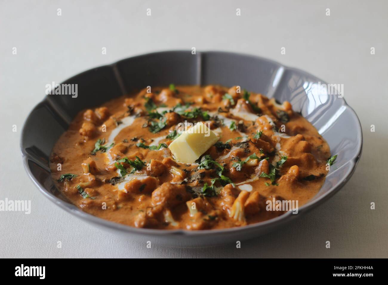 Gerösteter Blumenkohl mit Tomaten- und Cashewsoße. Eine beliebte Beilage aus Nordindien, die im Volksmund als gobi Butter Masala bekannt ist. Aufgenommen auf weißem Hintergrund Stockfoto