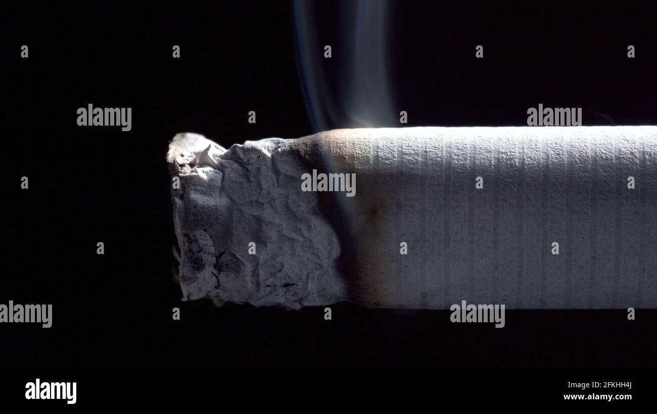 Foto einer schwelenden Zigarette mit Filter auf Schwarz Stockfoto