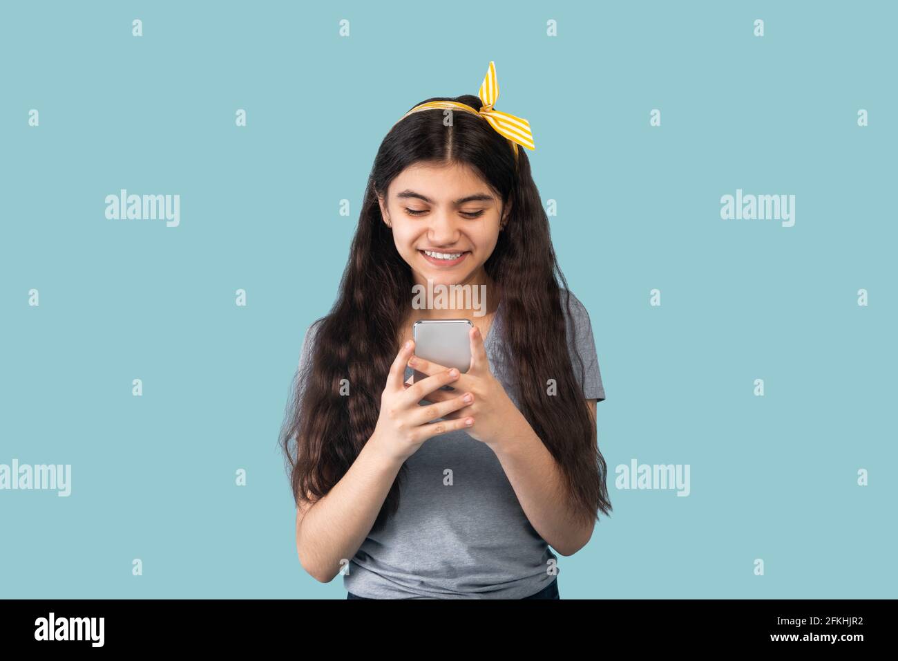 Menschen und Technologie. Porträt eines glücklichen lächelnden indischen Teenagers mit Smartphone über blauem Studiohintergrund Stockfoto