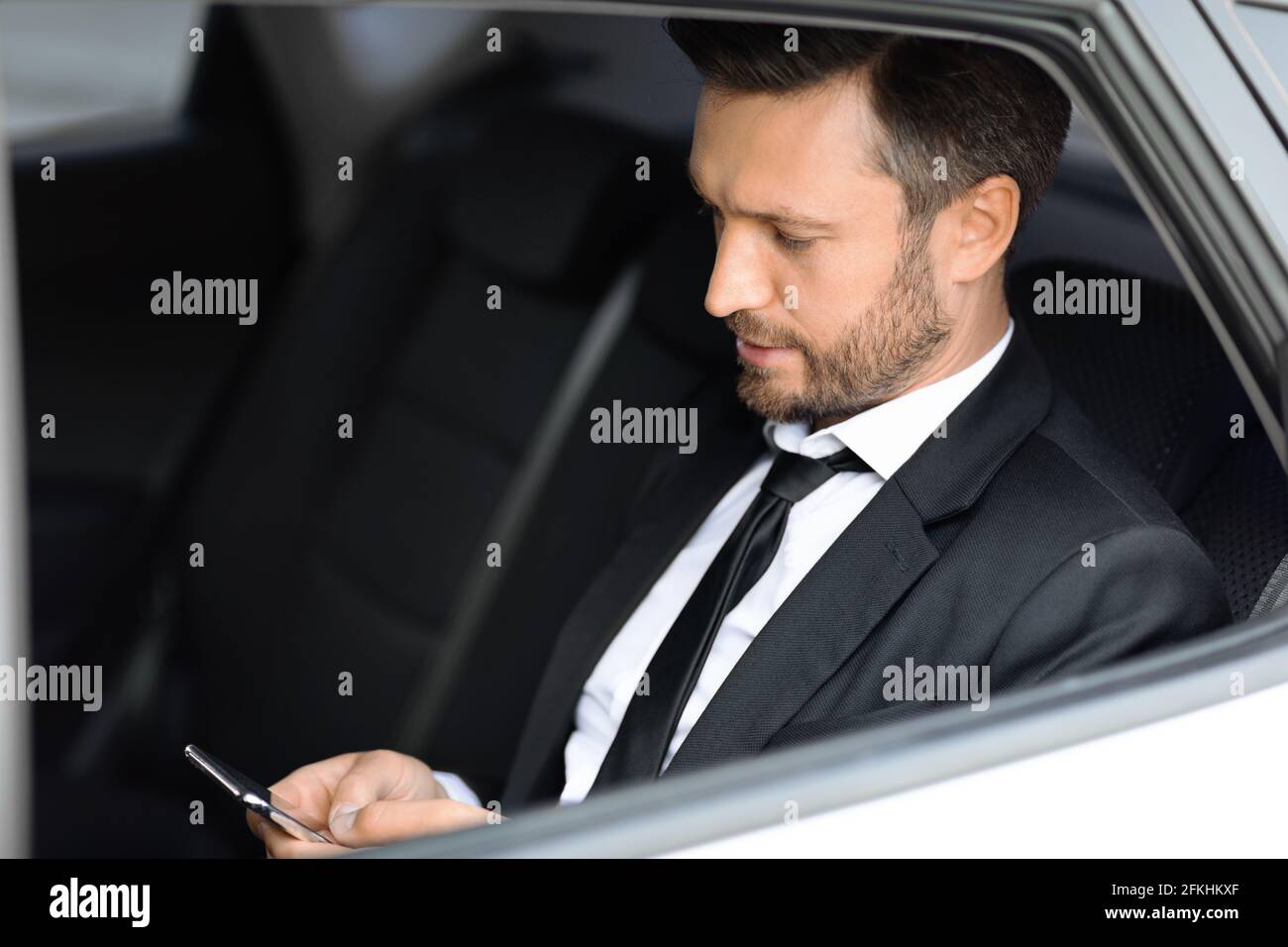 Wohlhabender Manager sitzt im Auto und benutzt Smartphone Stockfoto