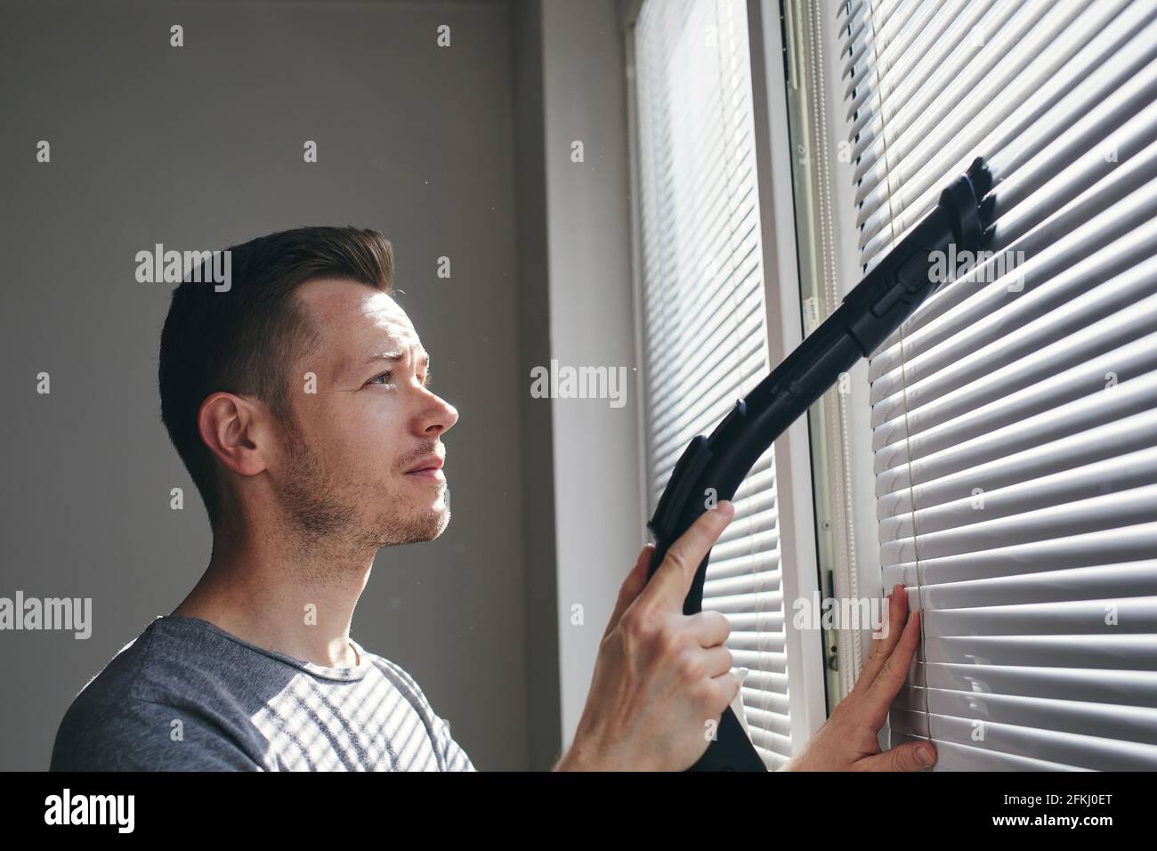 Mann, der zu Hause mit dem Staubsauger Staub von der Fensterblende reinigt. Themen Hausarbeit und Housekeeping. Stockfoto