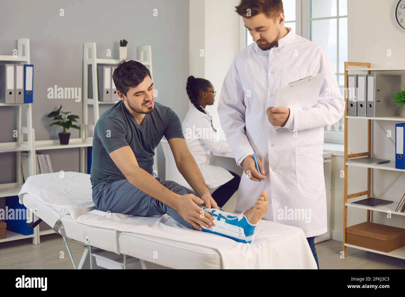 Junger Mann mit Knöchelverletzung, der sich beim Arzt über Schmerzen beschwert Und unbequem Korsett Stockfoto