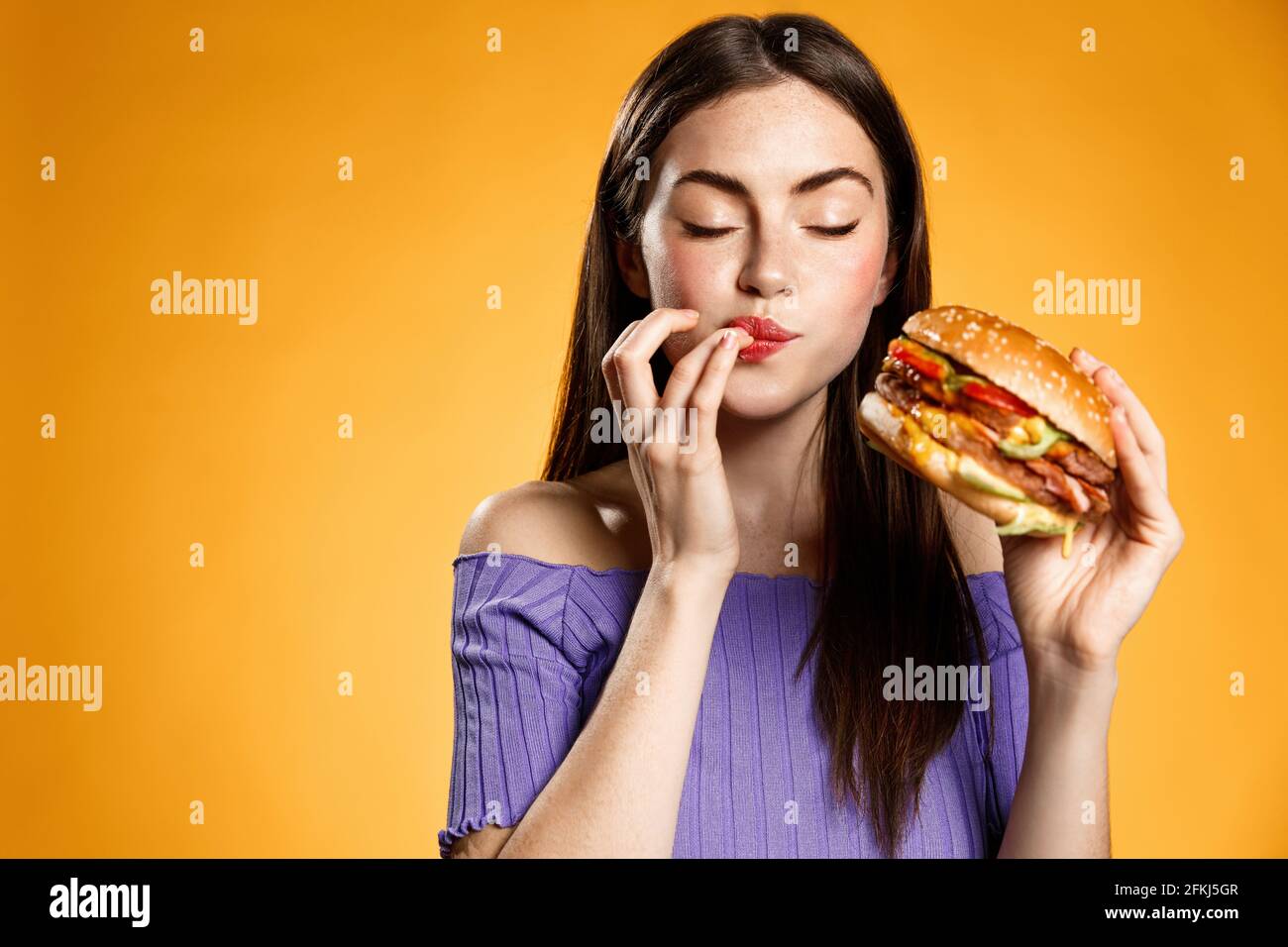 Frau essen Cheeseburger mit Zufriedenheit. Mädchen genießt leckere Hamburger zum Mitnehmen, leckt Finger leckeren Biss Burger, bestellen Fastfood Lieferung Stockfoto