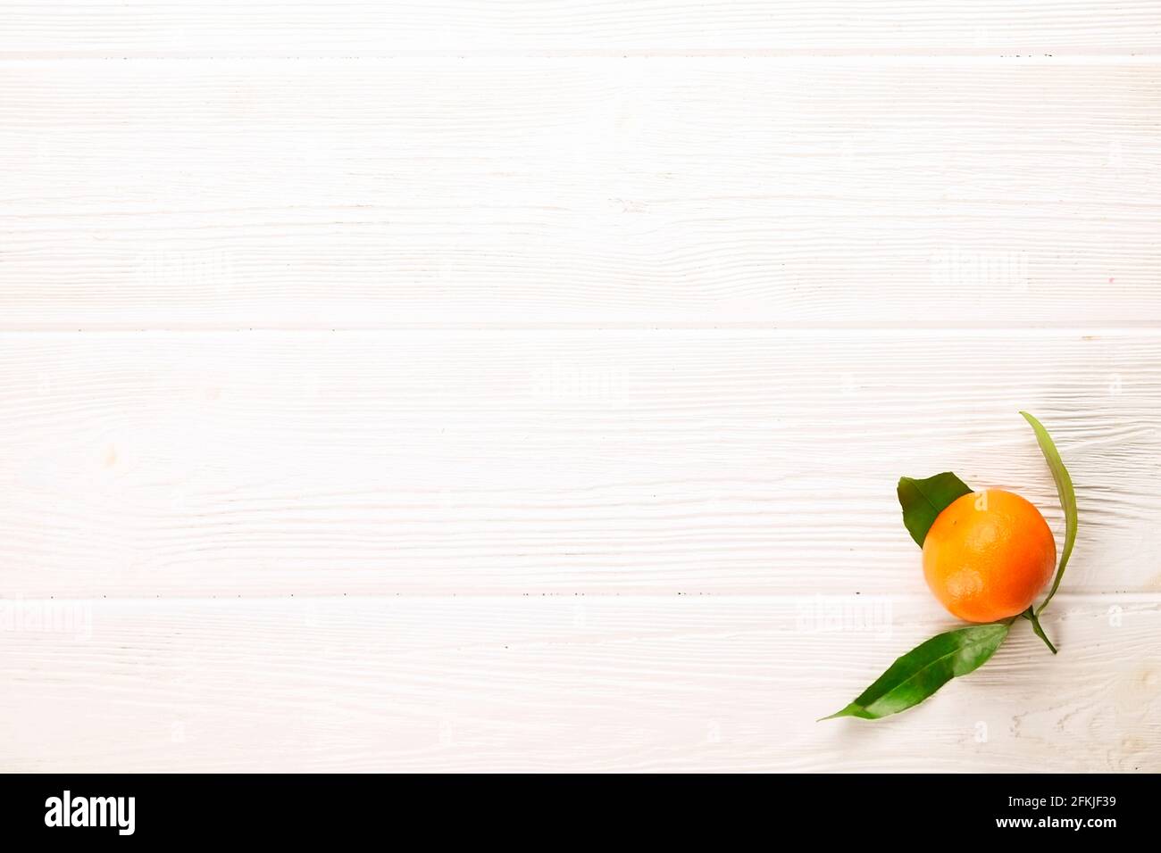 Einzelne frische ganze saftige Clementine orange mit Blättern auf weißem Holz strukturiert Tisch. Minimalistische Komposition aus gesunder, reifer Mandarine, roh vegan fo Stockfoto