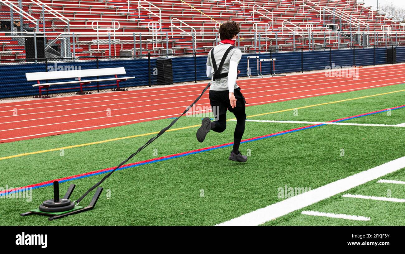 Ein High School-Läufer zieht einen Schlitten mit Gewichten auf ihm über ein grünes Rasenfeld während Strngth und Beweglichkeit üben. Stockfoto