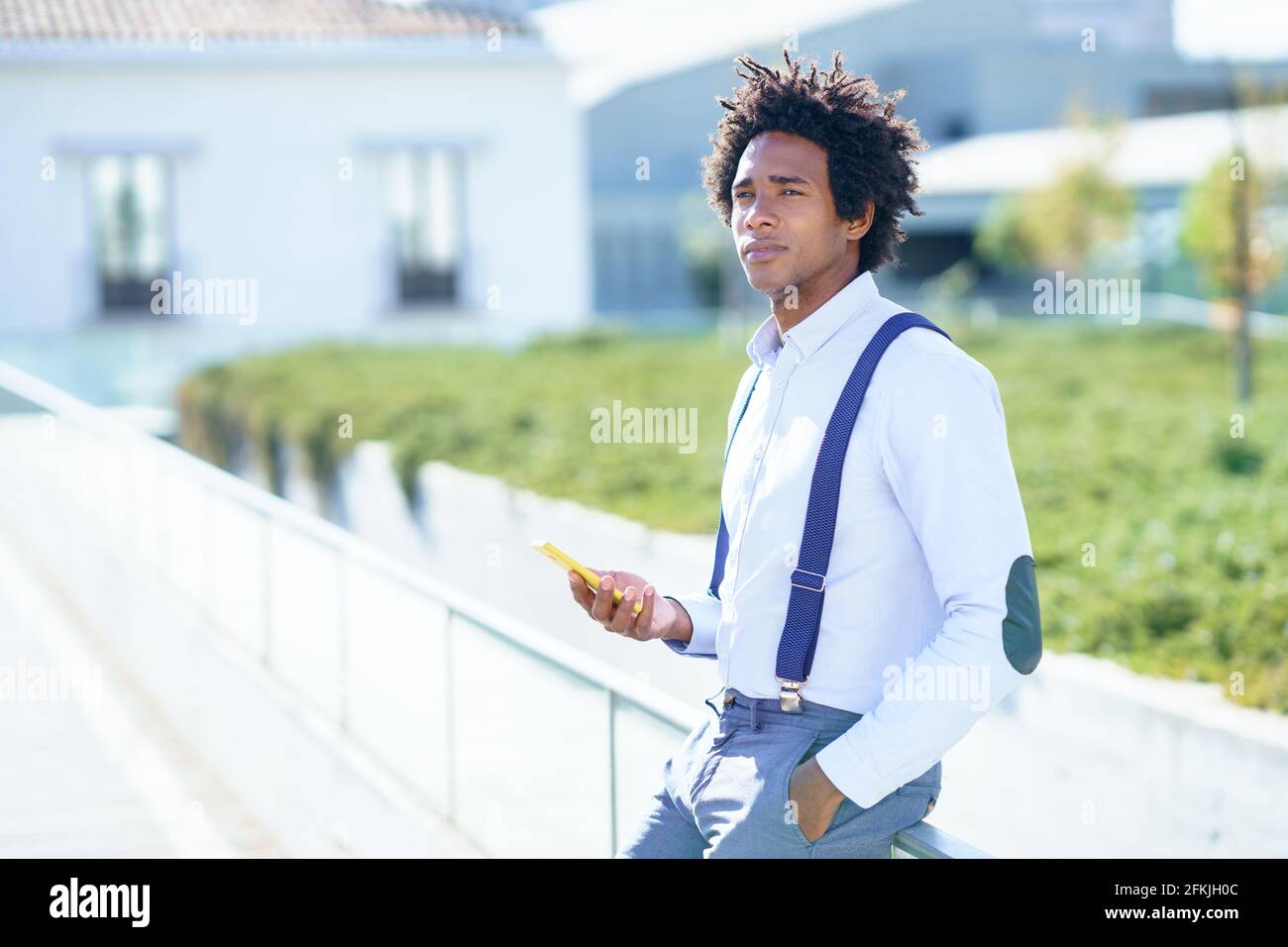 Schwarzer Mann mit Afro-Frisur mit einem Smartphone in der Nähe eines Bürogebäudes. Stockfoto