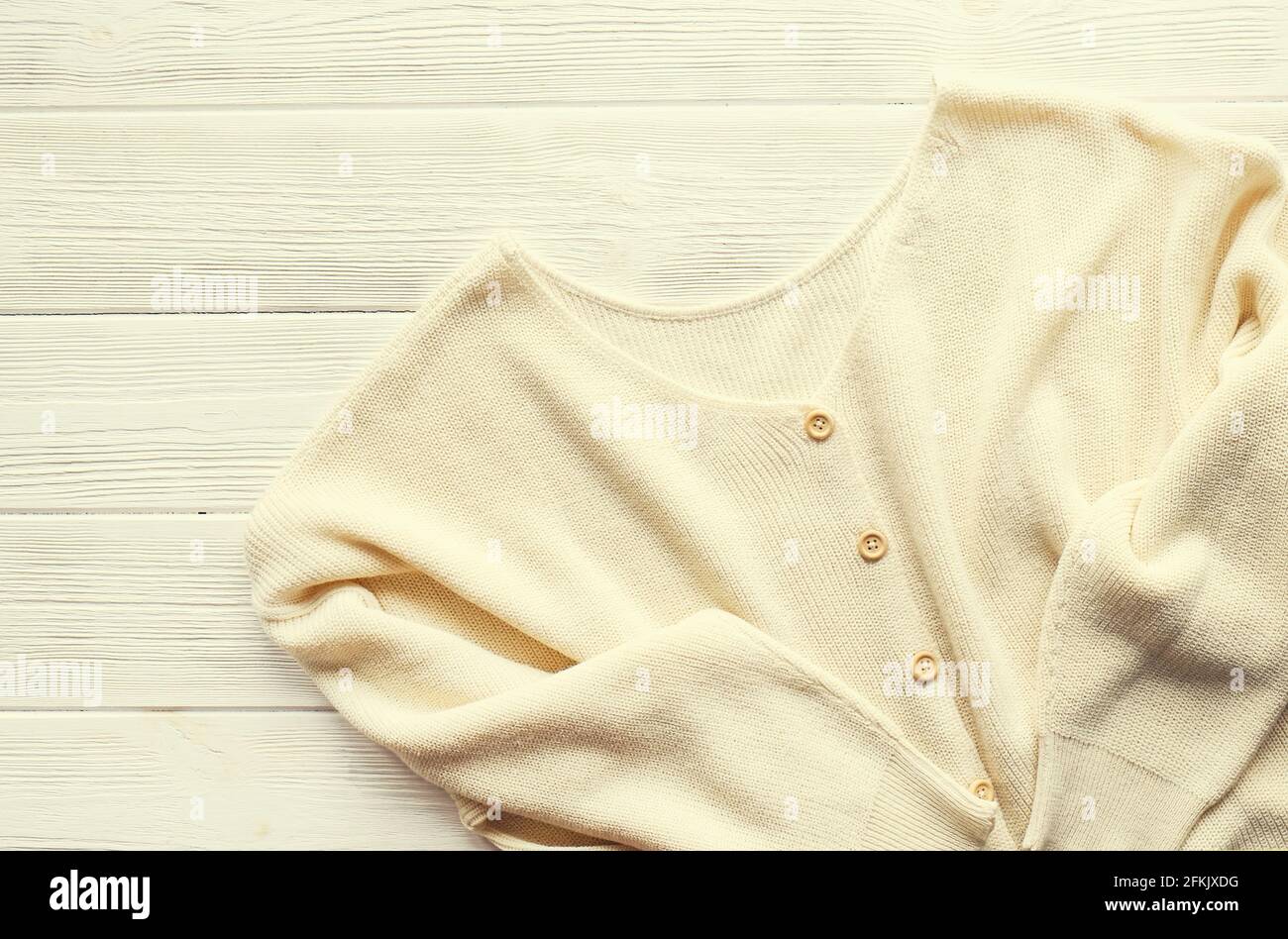 Modischer, schicker Pullover im lässigen Stil in Übergröße mit Knöpfen auf strukturiertem weißem Holz-Tischhintergrund. Draufsicht, Nahaufnahme, Kopierbereich. Stylisch Stockfoto