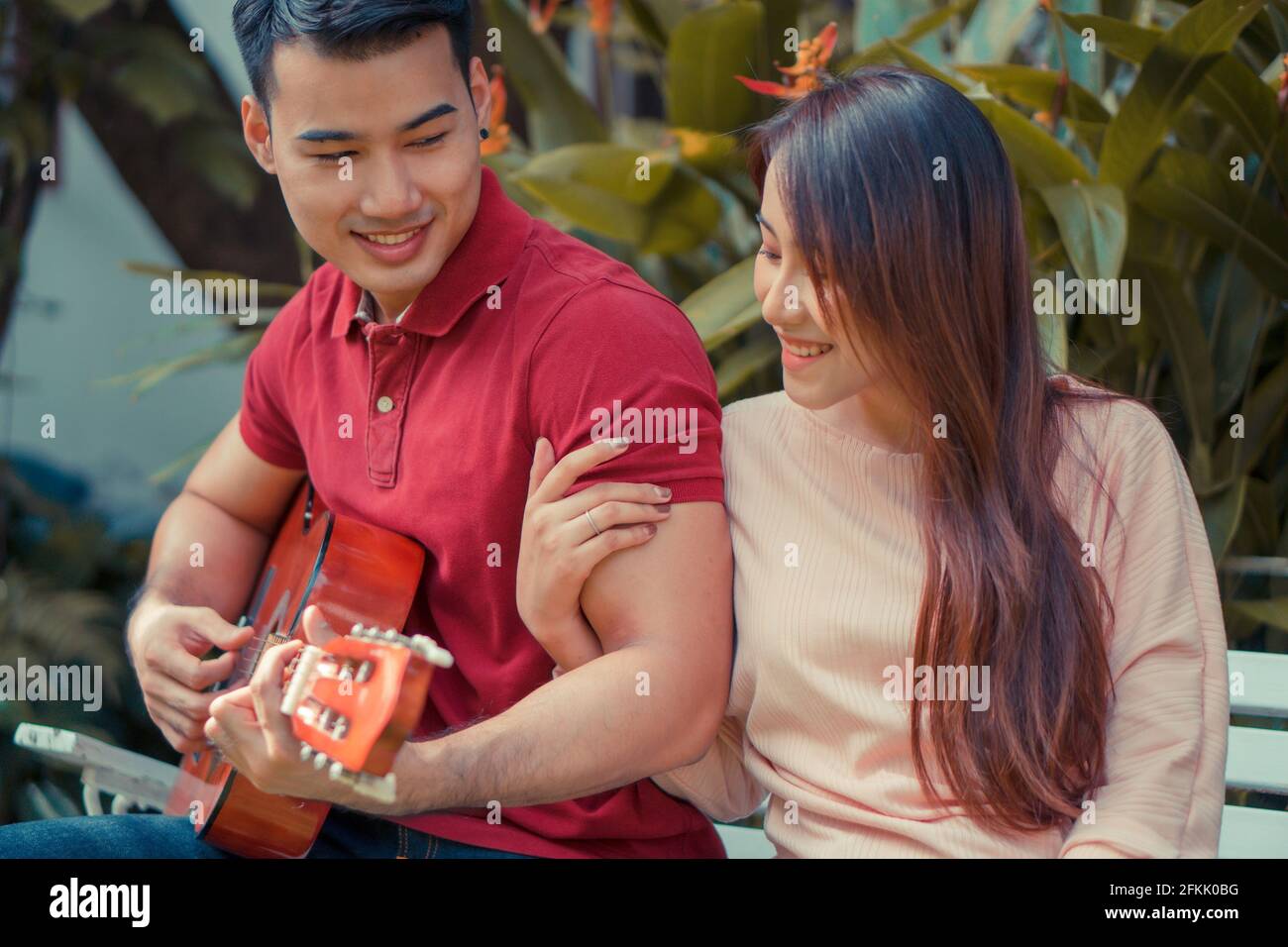 Glückliches junges verliebter Paare, die im Garten sitzen und Gitarre spielen und singen. Konzept von unvergesslichen und beeindruckenden Momenten Stockfoto