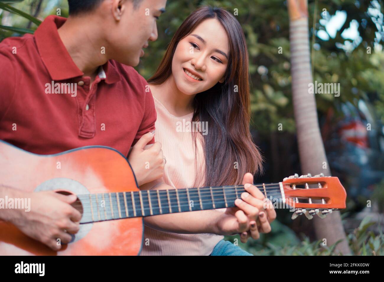 Glückliches junges verliebter Paare, die im Garten sitzen und Gitarre spielen und singen. Konzept von unvergesslichen und beeindruckenden Momenten Stockfoto