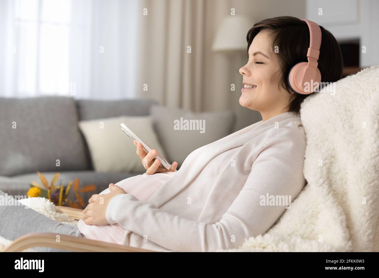 Junge Schwangere in Kopfhörern hören Musik auf dem Handy Stockfoto