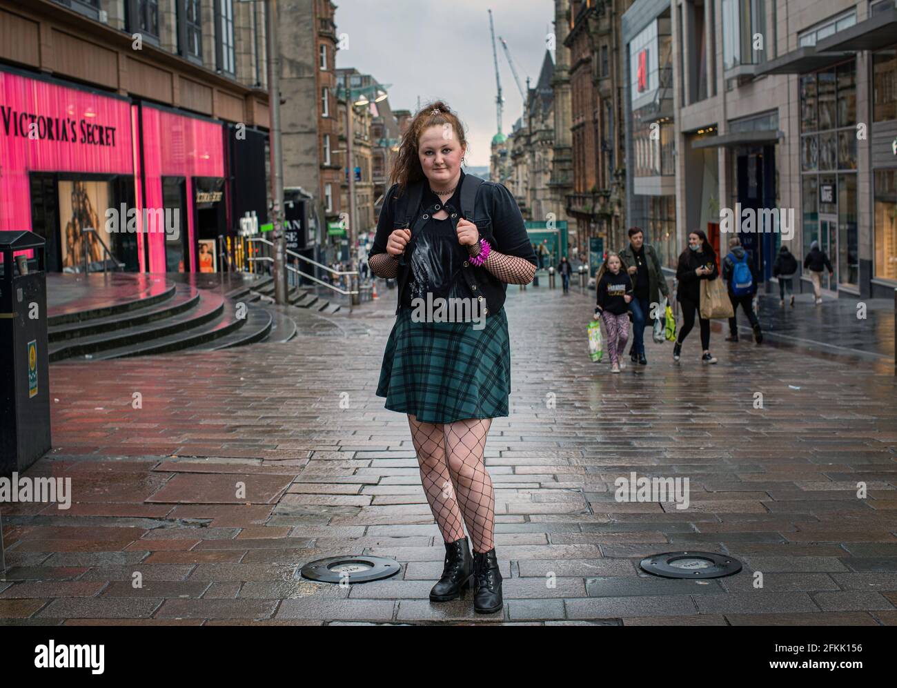 Potrait einer jungen Frau, die in einer leeren Einkaufsstraße in der Buchan Street im Zentrum von Glasgow, Schottland, einen Tartanrock und Netzstrümpfe trägt Stockfoto