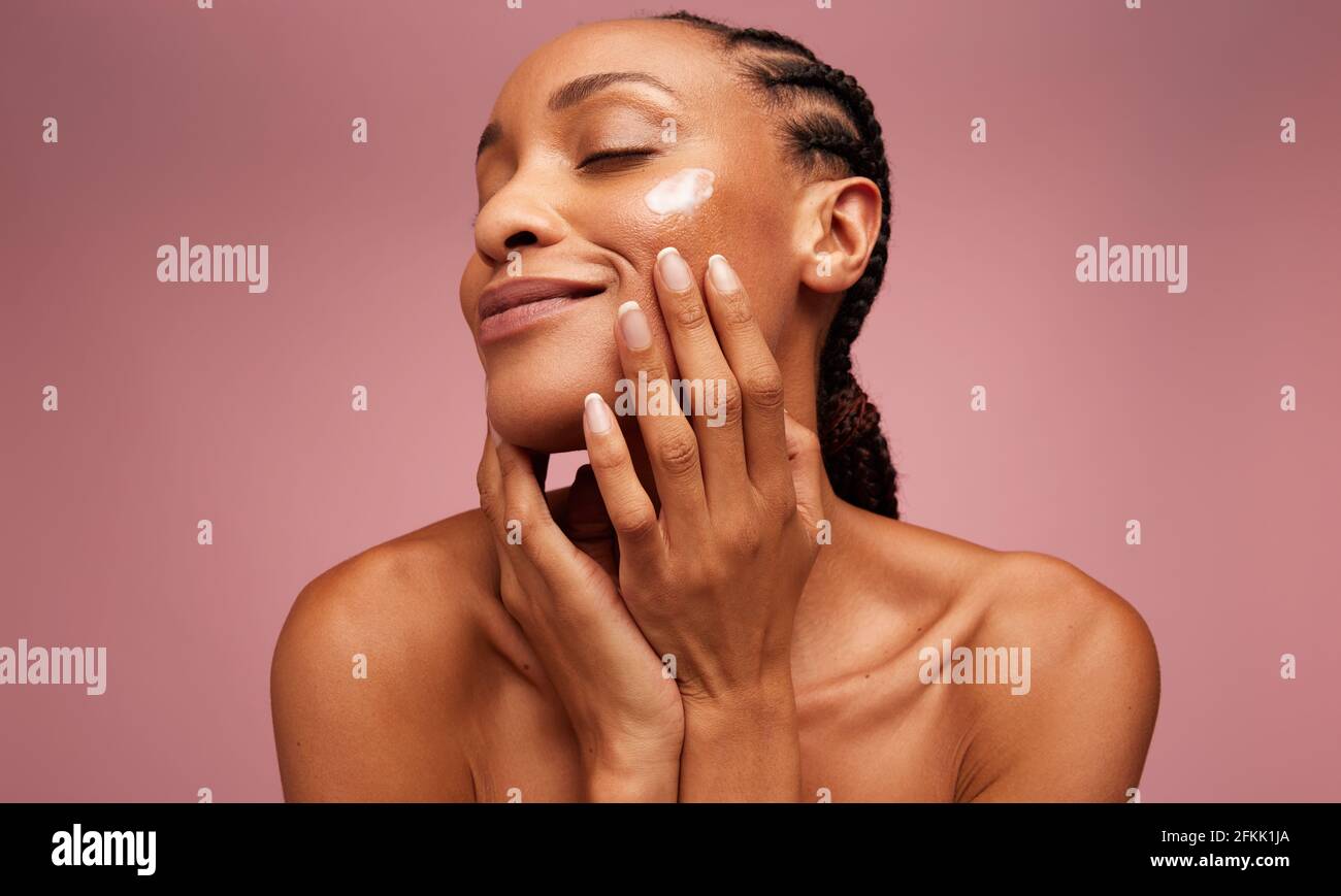 Nahaufnahme eines weiblichen Models, das ihr Gesicht mit einer Feuchtigkeitscreme versorgt. afroamerikanische Frau, die Feuchtigkeitscreme auf ihr Gesicht auftragen. Stockfoto