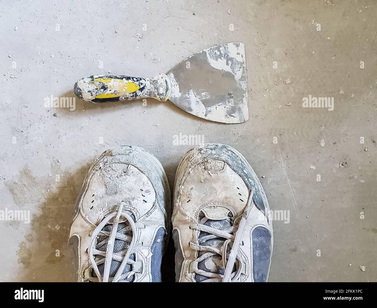 Alte schmutzige Arbeitsstiefel und ein Kittmesser auf Zement Etage - Blick von oben Stockfoto
