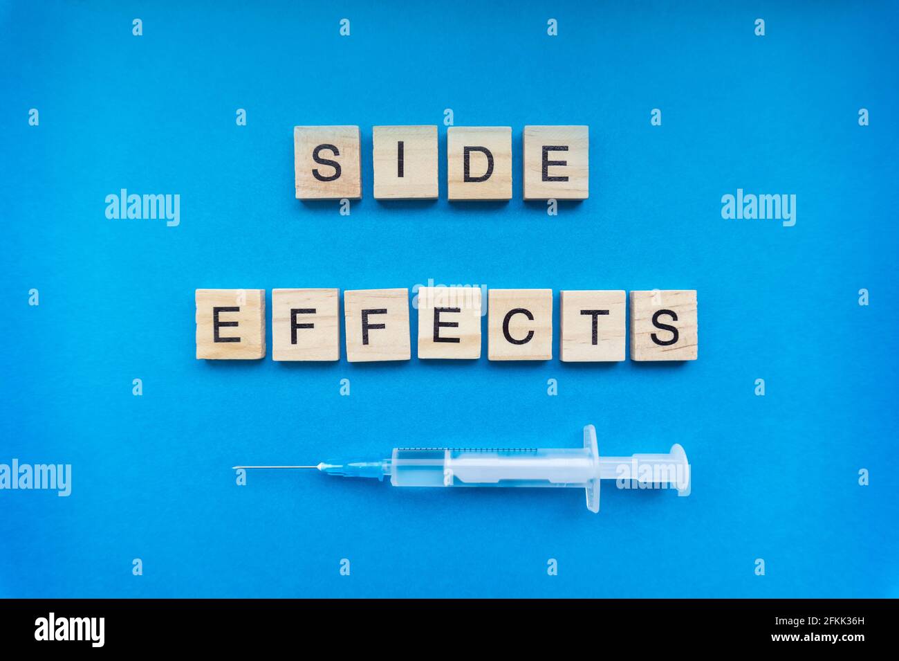 Nebenwirkungen-Schild mit Holzbuchstaben und einer Spritze auf blauem Hintergrund. COVID-19 Impfrisikokonzept Stockfoto