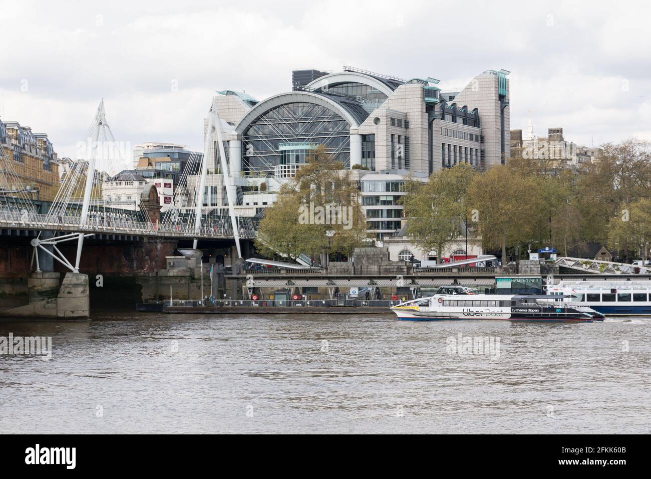 Ein Thames Clipper Uber Boat liegt am Victoria Embankment Landeplatz auf der Themse. Bahnhof Charing Cross im Hintergrund. Stockfoto