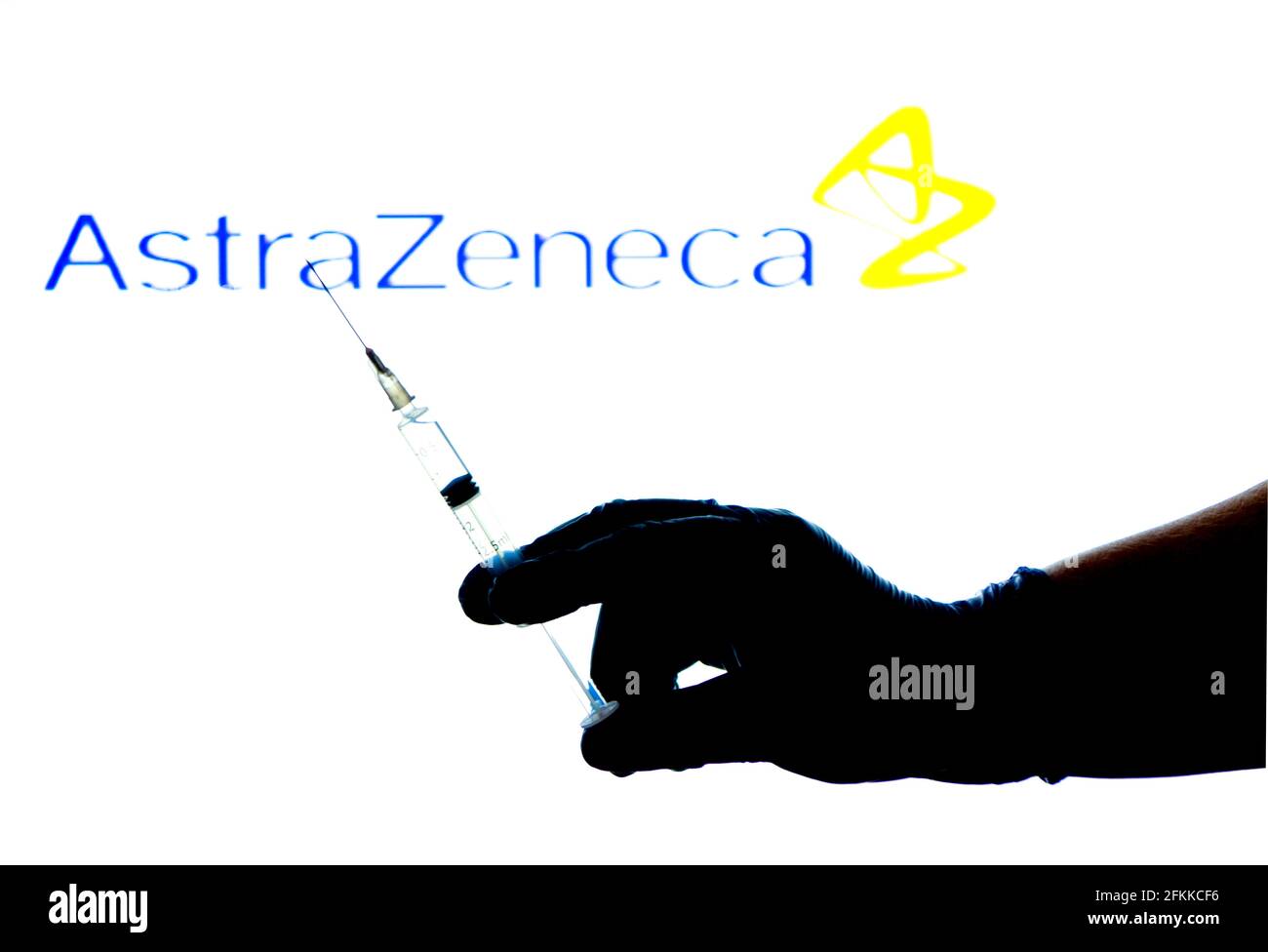 Madrid, Spanien - 2. Mai 2021: Hand-auf-Chirurgie-Handschuh mit Spritze mit Covid-Impfstoff. Im Hintergrund Logo von AstraZeneca Laboratory Stockfoto