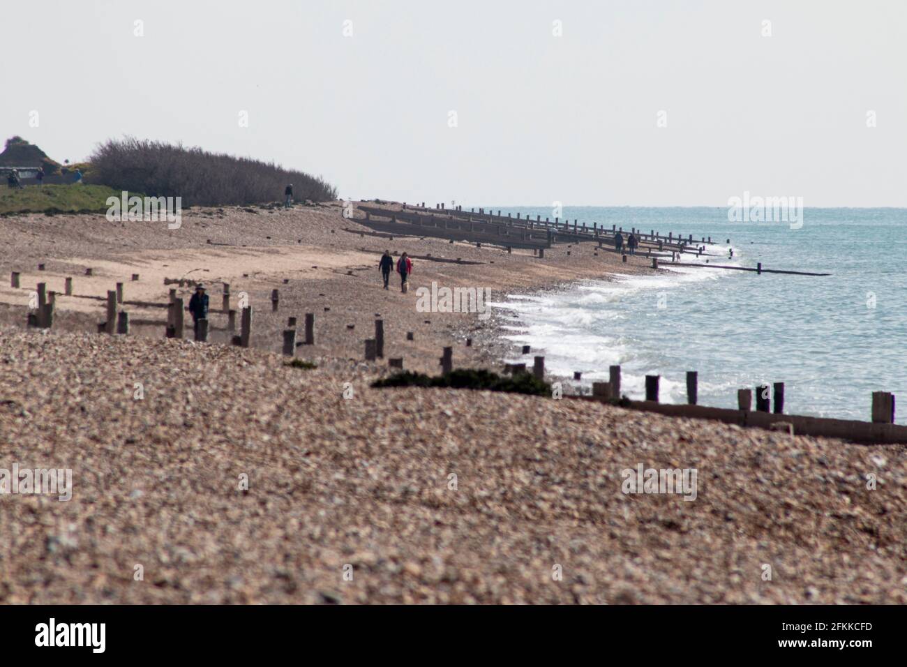 Nicht erkennbare Menschen, die an einem leeren Strand in West Sussex, Großbritannien, spazieren Stockfoto