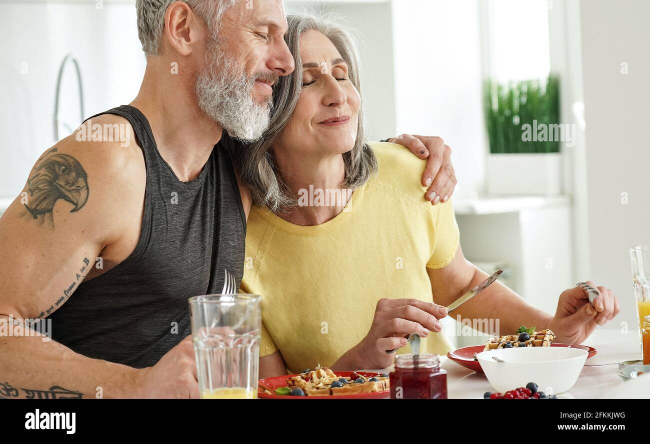 Glücklicher reifer Mann umarmt ältere Frau genießen das Frühstück zu Hause. Stockfoto