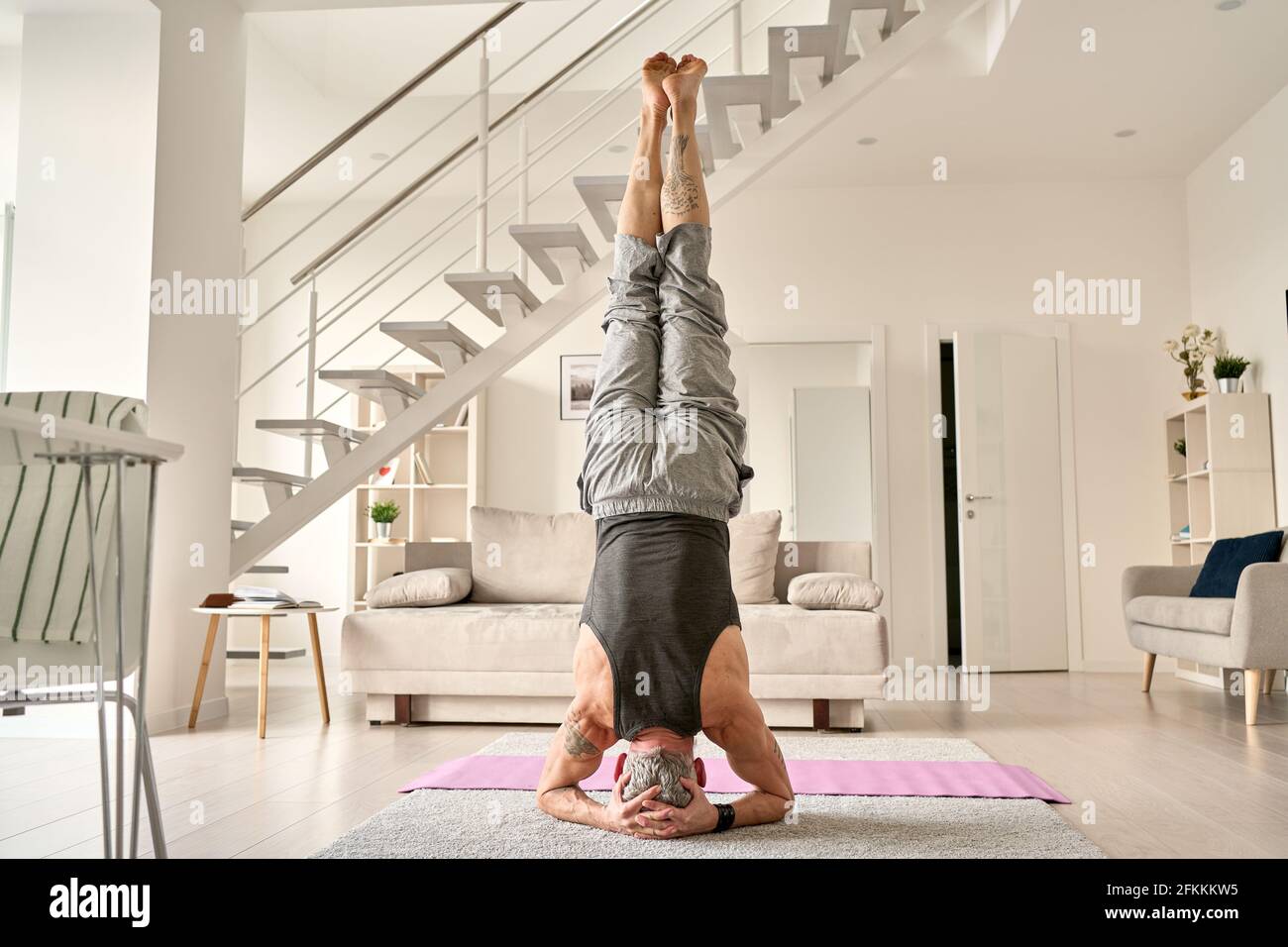 Fit mittleren Alters Senior tätowiert Mann macht Kopfstand Yoga-Übung zu Hause. Stockfoto